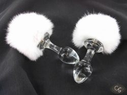 Two Crystal Delights glass butt plugs with white fluffy bunny tails on a black background