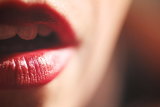 Close-up of a Dominant woman's parted lips wearing glossy red lipstick, with a glimpse of teeth