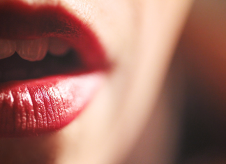 Close-up of a Dominant woman's parted lips wearing glossy red lipstick, with a glimpse of teeth