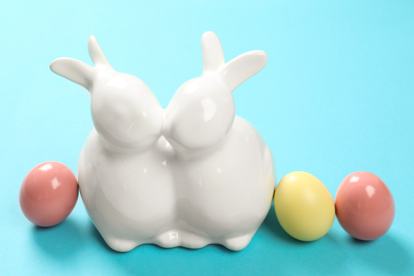 Ceramic Easter bunny couple kissing beside pastel eggs on a blue background