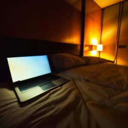 Laptop open on a bed in a dimly lit bedroom, set up for a private video call.