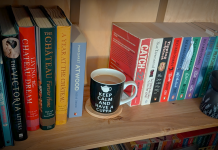 A warm wooden bookshelf with books on either side and a tea cup resting in the empty space where a book would normally sit