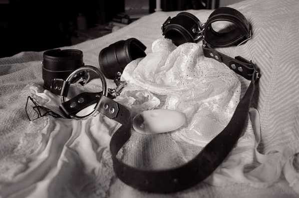 Leather cuffs and collar resting on soft bedding after a BDSM scene