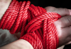 Red bondage rope restraining a submissive’s hands, symbolising BDSM consent, safety and power exchange