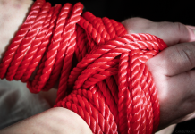 Red bondage rope restraining a submissive’s hands, symbolising BDSM consent, safety and power exchange