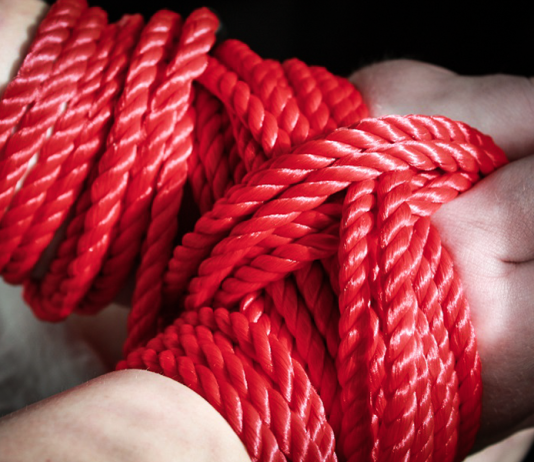 Red bondage rope restraining a submissive’s hands, symbolising BDSM consent, safety and power exchange