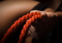 Hand gripping red bondage rope symbolising kink and fetish exploration
