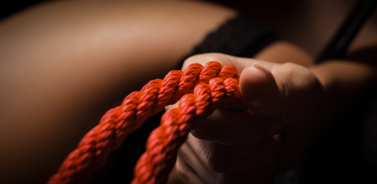 Hand gripping red bondage rope symbolising kink and fetish exploration