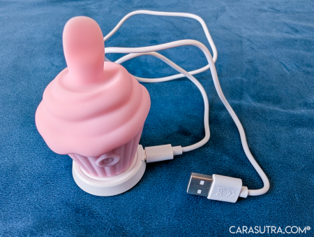 Pink Cupcake Vibrator standing upright on its white magnetic charging dock with USB-C wire attached, ready to charge