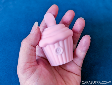 Pink Cupcake Vibrator held palm up in hand against blue backdrop, showing the small size and how it fits comfortably in the palm