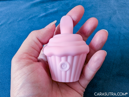 Pink Cupcake Vibrator resting in the palm of a hand against blue backdrop, showing the compact size for handheld use