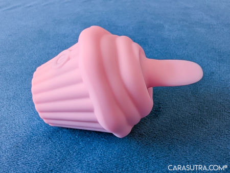 Pink Cupcake Vibrator lying on its side against blue carpet, showing the silicone tongue and the ridged cupcake case