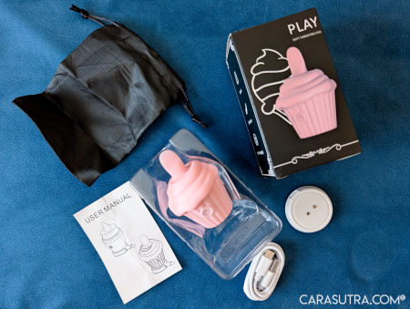 Cupcake Vibrator box contents laid out on blue velvet showing the black storage pouch, USB-C charging wire, instruction leaflet and white circular charging dock