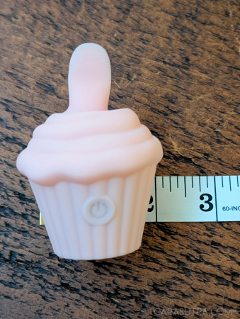 Pink Cupcake Vibrator on a dark wood surface next to a white measuring tape for scale