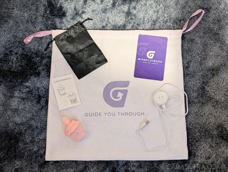 GITM Playbook branded fabric packaging bag with the Cupcake Vibrator, storage pouch, purple 'Guide You Through' booklet and charging cable arranged on top