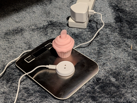 Pink Cupcake Vibrator on its charging dock connected to a mains USB adaptor, positioned on a flat surface for stable charging contact