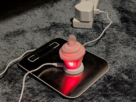 Pink Cupcake Vibrator charging on its dock with the red LED indicator lit behind the power button, confirming successful charging connection