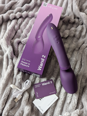 We-Vibe Wand 2 vibrator laid out with its packaging, USB charging cable and quick start guide on a grey blanket