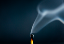 A just-extinguished match with wisps of smoke rising against a dark blue background
