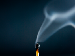 A just-extinguished match with wisps of smoke rising against a dark blue background