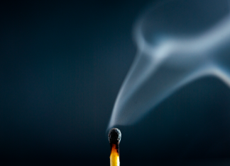Fatigue and Fire: Balancing Determination with Life’s Challenges A just-extinguished match with wisps of smoke rising against a dark blue background