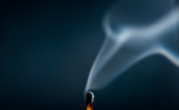 Fatigue and Fire: Balancing Determination with Life’s Challenges A just-extinguished match with wisps of smoke rising against a dark blue background