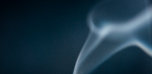 A just-extinguished match with wisps of smoke rising against a dark blue background