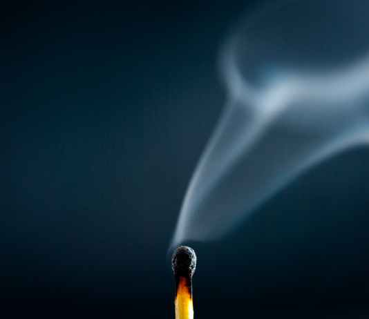 A just-extinguished match with wisps of smoke rising against a dark blue background