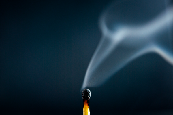 A just-extinguished match with wisps of smoke rising against a dark blue background