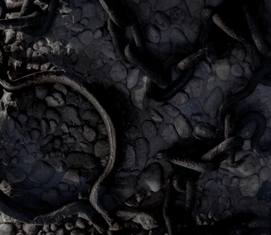 Rusted iron shackle and tangled chains on cold stone floor, cool-toned close-up