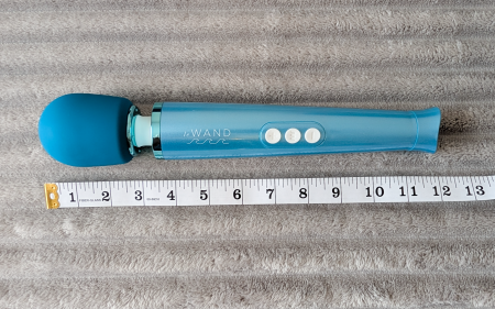 Le Wand Dive vibrator on a grey fluffy blanket, with a measuring tape laid by its side, showing its full length as 12 inches