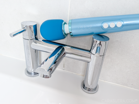 Le Wand Dive submersible wand vibrator balanced on top of chrome bath taps against a white tiled bathroom wall, showing waterproof design
