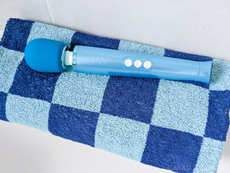 Le Wand Dive wand vibrator laid across a folded blue and white checkerboard patterned bath towel on a tiled floor