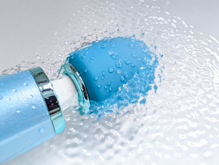 Close-up of the Le Wand Dive head being splashed with water, droplets covering the silicone head and chrome collar demonstrating the IPX8 waterproof rating