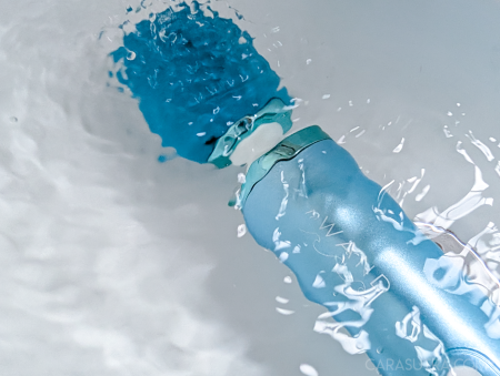 Le Wand Dive wand vibrator held under the bathwater at an angle, silicone head submerged with water flowing around it, showing full IPX8 submersion in action