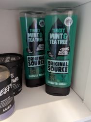 Two bottles of Original Source Mint & Tea Tree Shower Gel on a bathroom shelf, with the edges of two Lush bath products visible