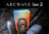 Arcwave Ion 2 review feature image showing the black Pleasure Air suction stroker standing upright beside its retail box, with the black neoprene zip storage pouch and magnetic charging cable laid out on a black blanket