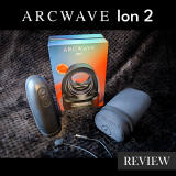 Arcwave Ion 2 review feature image showing the black Pleasure Air suction stroker standing upright beside its retail box, with the black neoprene zip storage pouch and magnetic charging cable laid out on a black blanket
