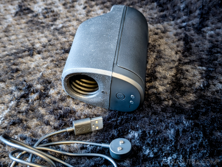 Arcwave Ion 2 laid on a black blanket showing the entrance of the silicone sleeve at the base as well as the magnetic charging connectors, with its magnetic to USB charging wire coiled nearby